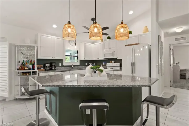 Kitchen featuring a breakfast bar, decorative light fixtures, white cabinets, dark stone countertops, and lofted ceiling