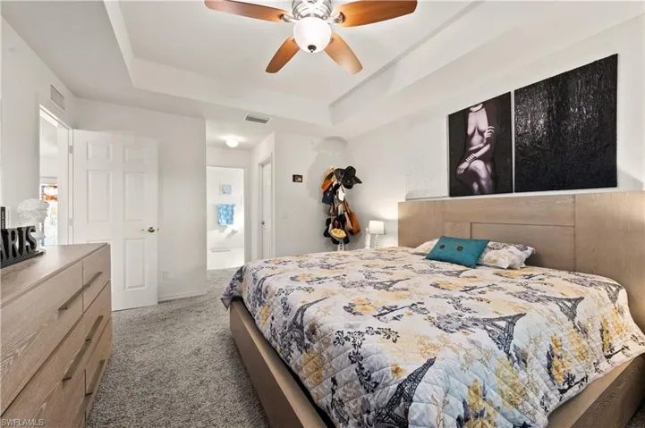Bedroom with light colored carpet, a raised ceiling, a ceiling fan, and connected bathroom