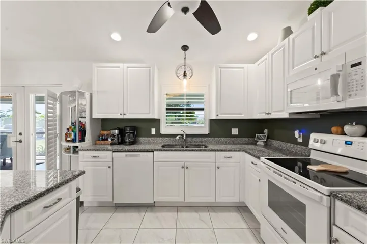 Kitchen featuring white appliances, white cabinetry, dark stone counters, pendant lighting, and a ceiling fan