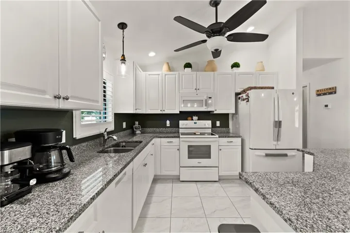 Kitchen featuring white appliances, lofted ceiling, dark stone counters, white cabinetry, and recessed lighting