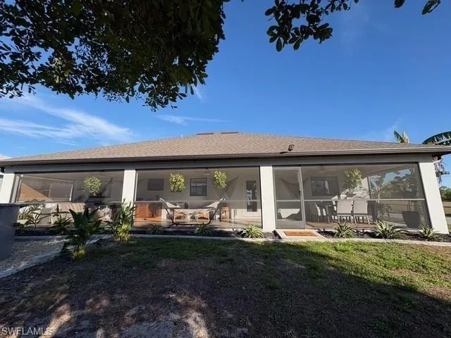 Back of house featuring a sunroom, roof with shingles, and a yard
