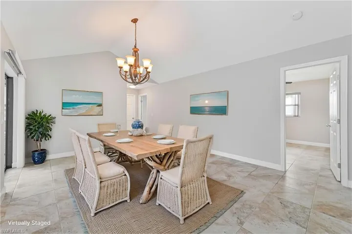 Dining area featuring vaulted ceilings, a central chandelier, and large format tile flooring