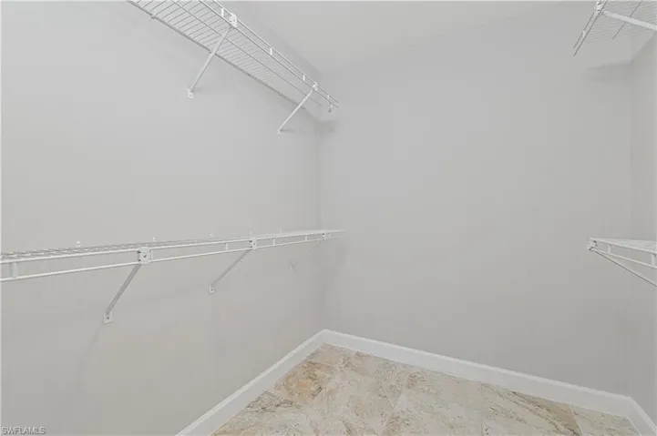 Walk-in closet featuring light gray walls, white wire shelving, and neutral-toned tile flooring