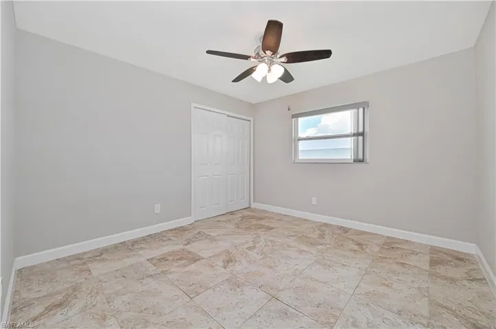 Spacious room featuring neutral wall tones, large format tile flooring, a window with horizontal blinds, a ceiling fan with integrated lighting, and a white bi-fold closet door