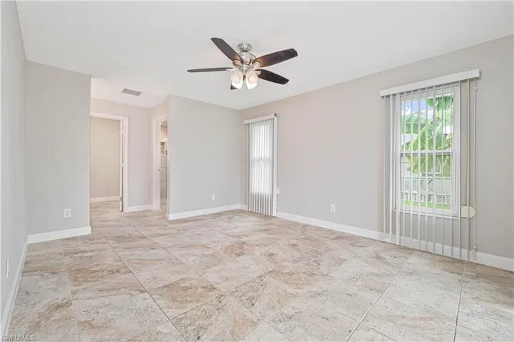 Spacious room featuring neutral wall tones, large format tile flooring, a ceiling fan with integrated lighting, and multiple windows with vertical blinds