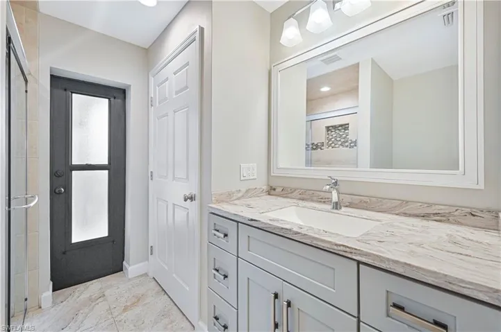 Bathroom featuring a light-toned vanity with an integrated sink, a framed mirror, and a three-light fixture