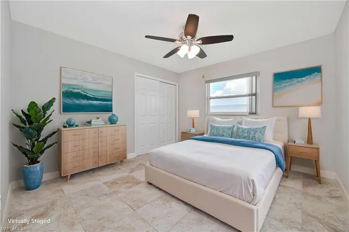Bedroom featuring large format tile flooring, a window with a roller shade, a ceiling fan with integrated lighting, and white bi-fold closet doors
