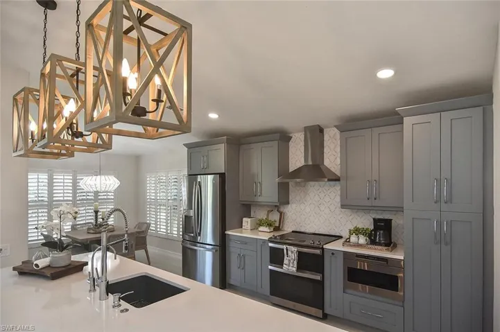 Kitchen featuring hanging light fixtures, stainless steel appliances, wall chimney range hood, decorative backsplash, and light Quartz countertops