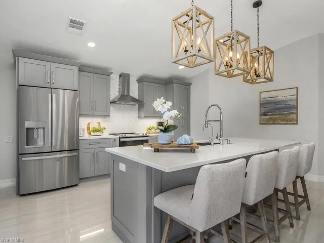 Kitchen featuring stainless steel appliances, backsplash, gray cabinets, a breakfast bar area, Quartz countertops, and wall chimney range hood