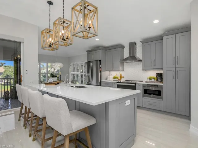 Kitchen with a kitchen bar, Quartz countertops, backsplash, wall chimney exhaust hood, decorative light fixtures, and appliances with stainless steel finishes