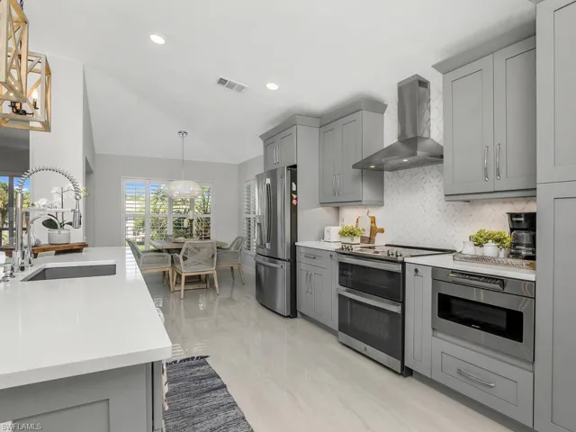 Kitchen with appliances with stainless steel finishes, wall chimney range hood, decorative backsplash, Quartz countertops, hanging light fixtures, and gray cabinets