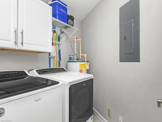 Washroom featuring electric panel, cabinet space, washer and clothes dryer, and water heater