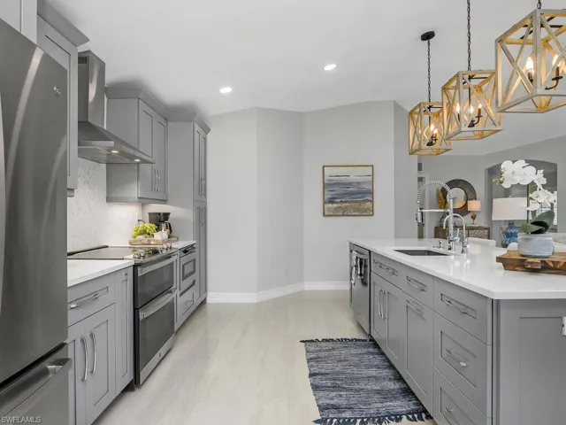 Kitchen with gray cabinets, wall chimney exhaust hood, appliances with stainless steel finishes, and recessed lighting