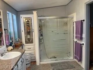 Bathroom with a textured ceiling, vanity, a stall shower, and wood finished floors