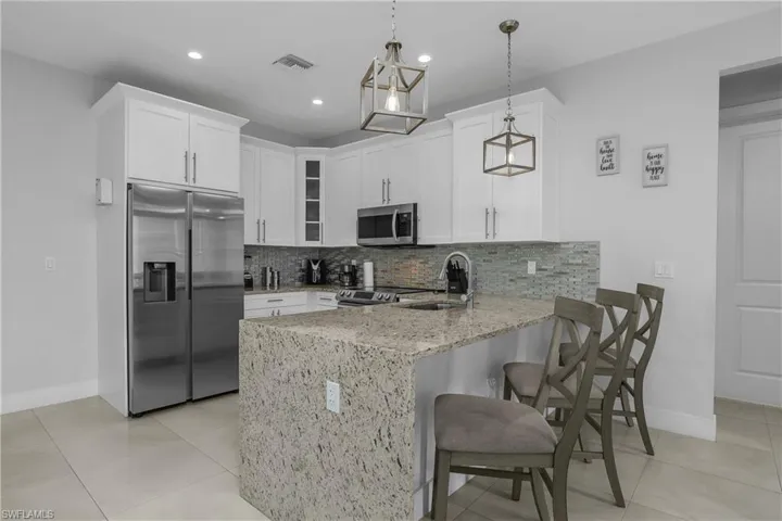 The kitchen features white cabinetry, a large stainless steel refrigerator, a granite countertop island with seating, and recessed lighting