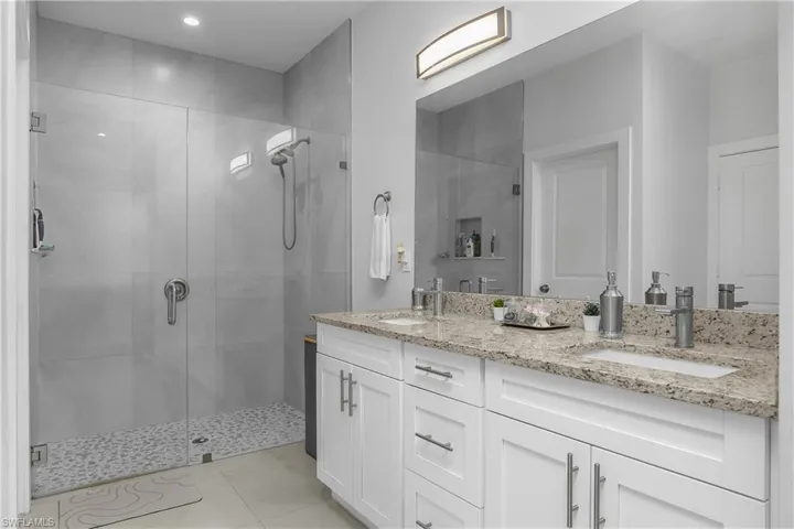 Bathroom featuring a spacious walk-in shower with a glass enclosure, a dual vanity with light-colored granite countertops, and white cabinetry with brushed nickel hardware