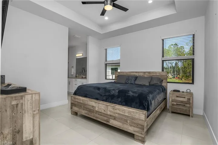 This bedroom features light-colored tile flooring, a ceiling fan, and two windows with horizontal blinds