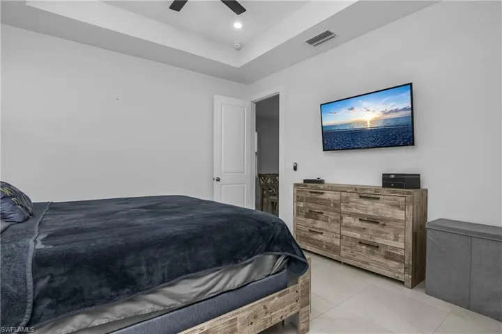 This room features a ceiling fan, tray ceiling, and light-colored tile flooring