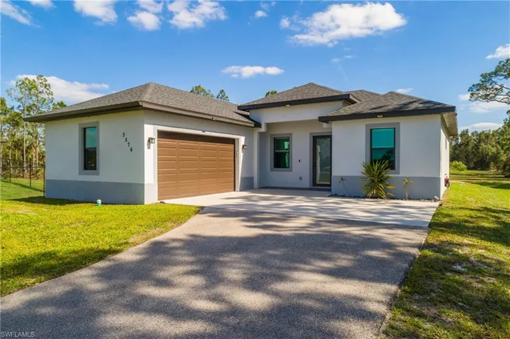 The property features a concrete driveway, an attached garage with a brown door, and a well-maintained lawn