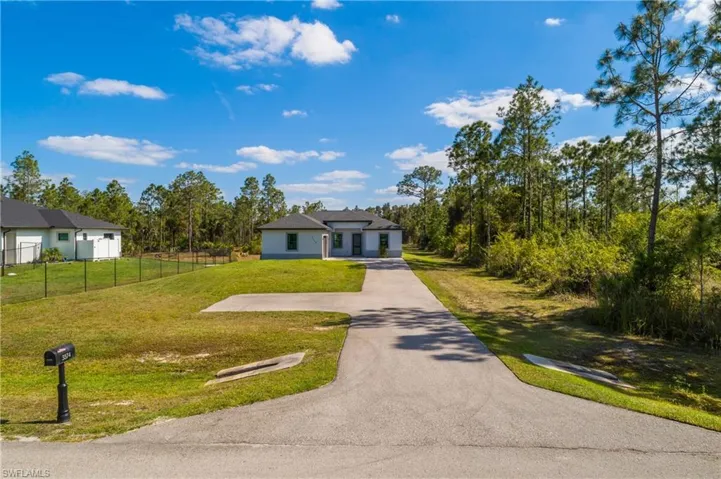 The property features a long paved driveway leading to the residence, surrounded by a natural landscape with mature trees
