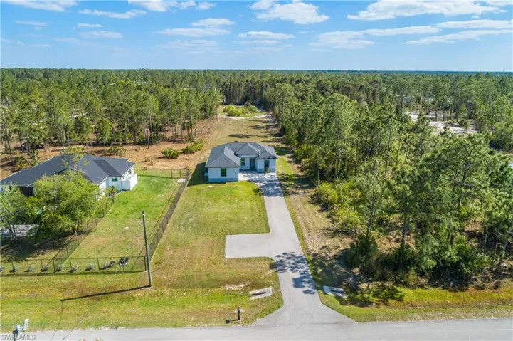 The property features a single-story home with a gray roof and light-colored exterior, situated on a grassy lot with a paved driveway