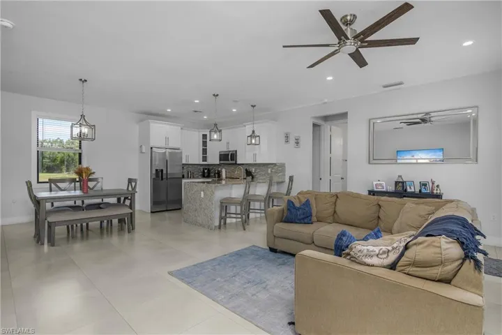 Bright and spacious open-plan living area featuring light-colored tile flooring, recessed lighting, and a modern ceiling fan