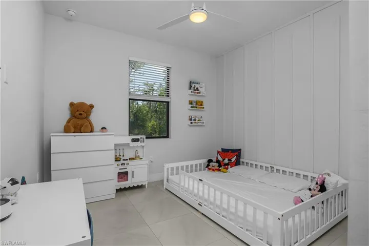 Bedroom with light-colored tile flooring, a window offering exterior views, and a ceiling fan with integrated lighting