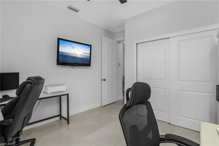 This room features light-colored tile flooring, a wall-mounted television, and a white sliding door closet