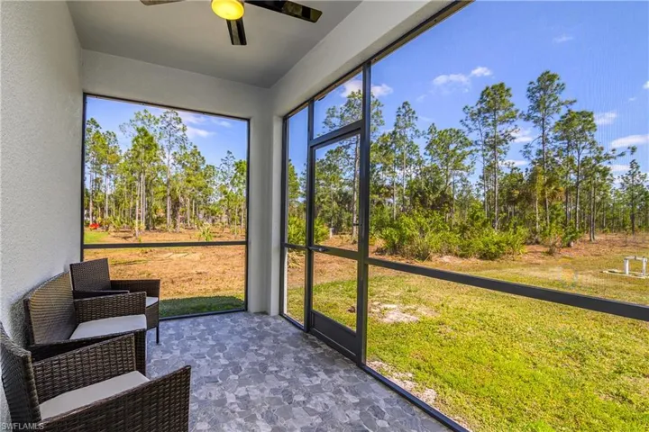Screened patio with a tiled floor and a ceiling fan, overlooking a spacious yard with mature trees