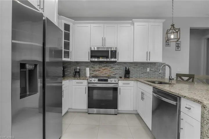 Well-appointed kitchen featuring white cabinetry, granite countertops, and stainless steel appliances, including a refrigerator, oven, microwave, and dishwasher