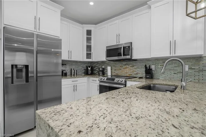 The kitchen features granite countertops, white cabinetry, a tiled backsplash, and stainless steel appliances including a refrigerator, microwave, and range