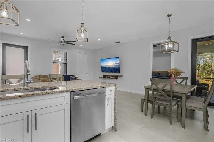 The open concept living area includes a kitchen island with granite countertops, a stainless steel dishwasher, and a dining area with a four-person table