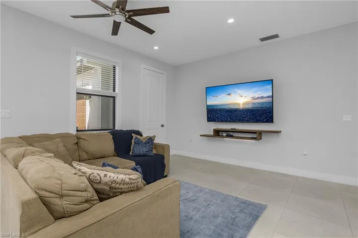 Living area featuring light-colored tile flooring, a ceiling fan, recessed lighting, and a window with blinds