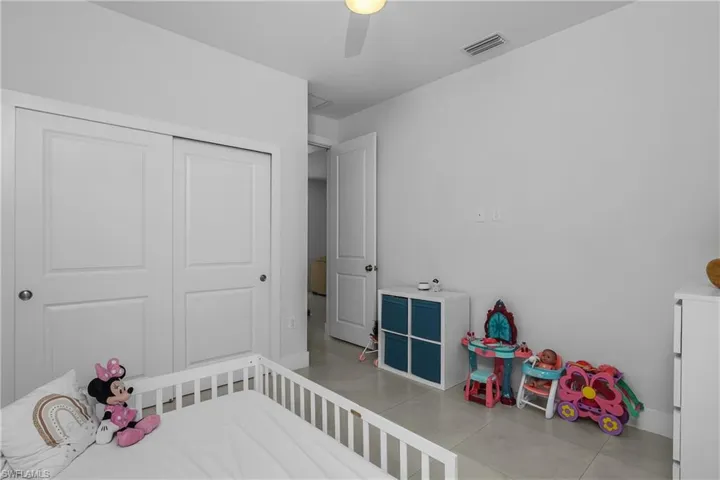 This room features a ceiling fan, light-toned tile flooring, and white walls