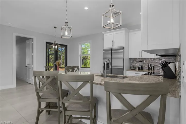 The kitchen features white cabinetry, a stainless steel refrigerator, and a tiled backsplash