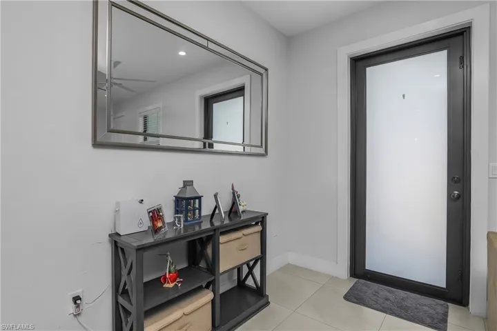 Entryway featuring a dark-framed door with a frosted glass panel, light-colored tile flooring, and a large rectangular mirror on the wall