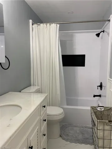 Bathroom featuring vanity, shower / bathtub combination with curtain, and light marble finish floors