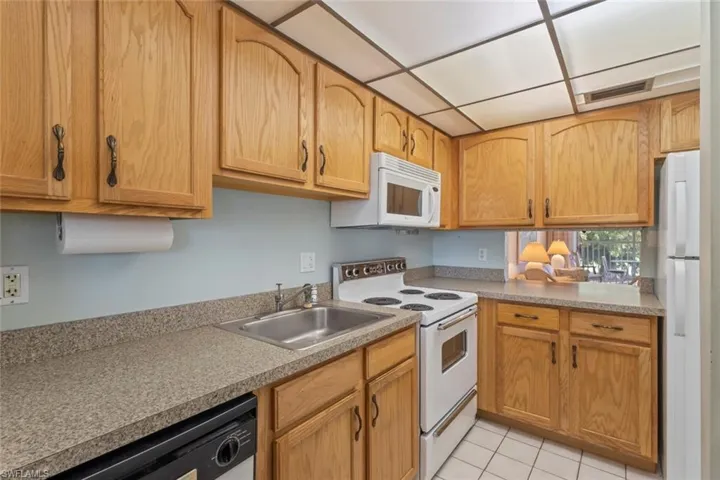 Kitchen with white appliances, light tile patterned floors, light countertops, and a paneled ceiling
