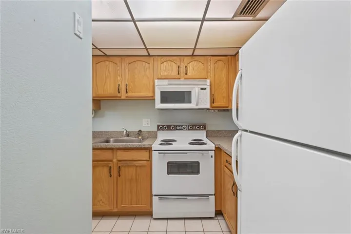 Kitchen with white appliances, light tile patterned flooring, light countertops, and a textured wall
