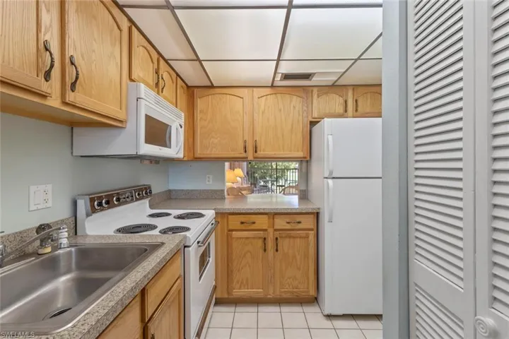 Kitchen featuring white appliances, light tile patterned flooring, light countertops, and a drop ceiling