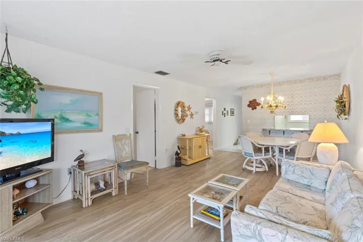 Living room featuring a ceiling fan, light wood-type flooring, a chandelier, and an accent wall