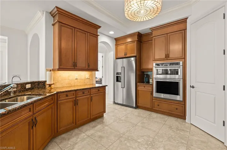 Kitchen featuring a sink, brown cabinetry, stainless steel appliances, arched walkways, and dark stone counters