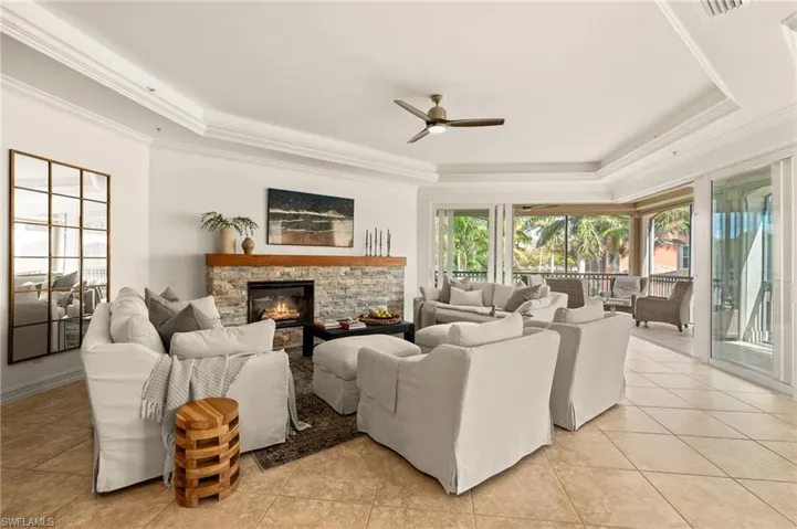 Living area featuring a stone fireplace, ceiling fan, crown molding, and a raised ceiling