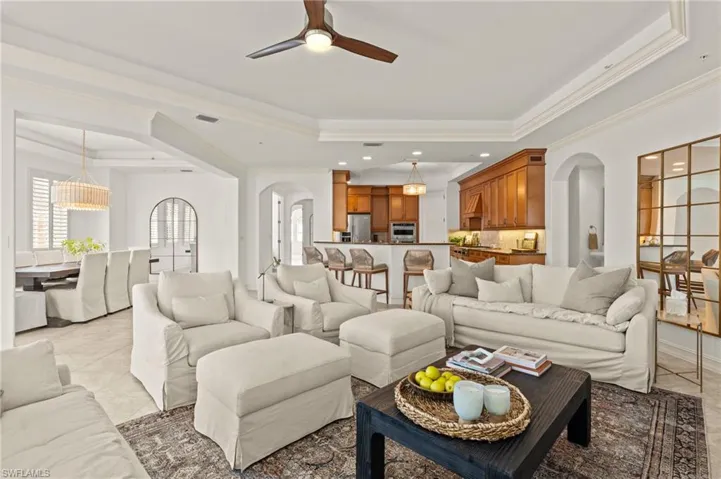 Living room with arched walkways, ornamental molding, ceiling fan with notable chandelier, and a raised ceiling