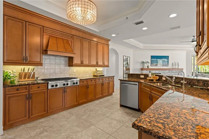 Kitchen with custom exhaust hood, appliances with stainless steel finishes, a tray ceiling, and visible vents