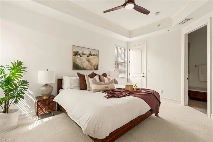 Carpeted bedroom with visible vents, baseboards, ornamental molding, a raised ceiling, and ensuite bath
