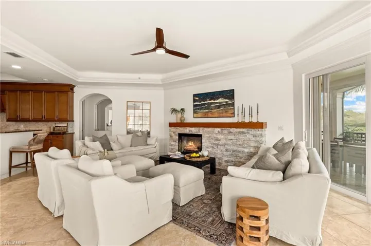 Living area featuring crown molding, arched walkways, ceiling fan, visible vents, and a stone fireplace