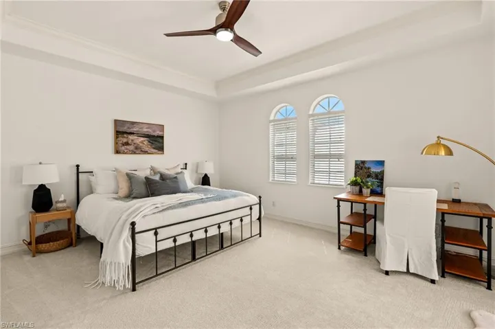 Carpeted bedroom featuring a raised ceiling, crown molding, baseboards, and ceiling fan