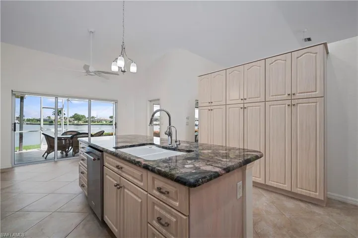 Kitchen with ceiling fan with notable chandelier, a center island with sink, pendant lighting, sink, and dark stone countertops