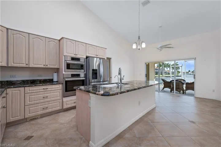 Kitchen featuring a center island with sink, hanging light fixtures, stainless steel appliances, high vaulted ceiling, and dark stone countertops